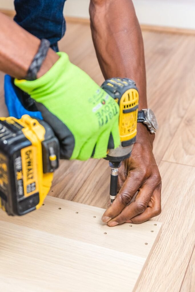 Close-up of handyman drilling wood indoors with green gloves and cordless drill.